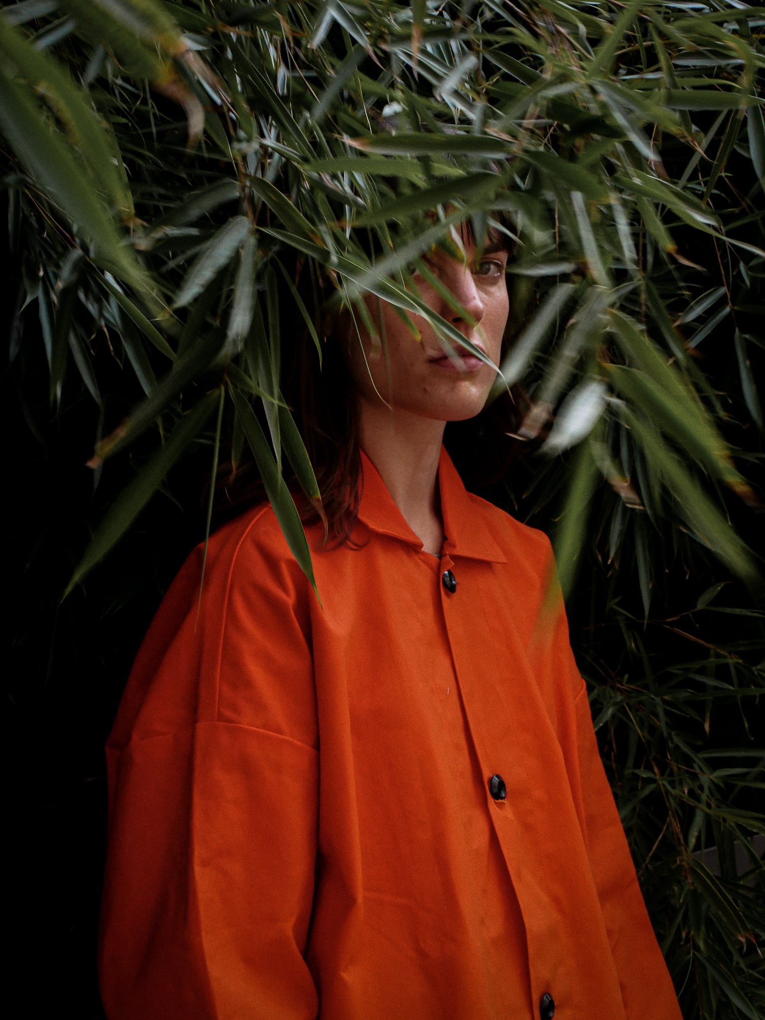 Person wearing an orange jacket standing among green leaves