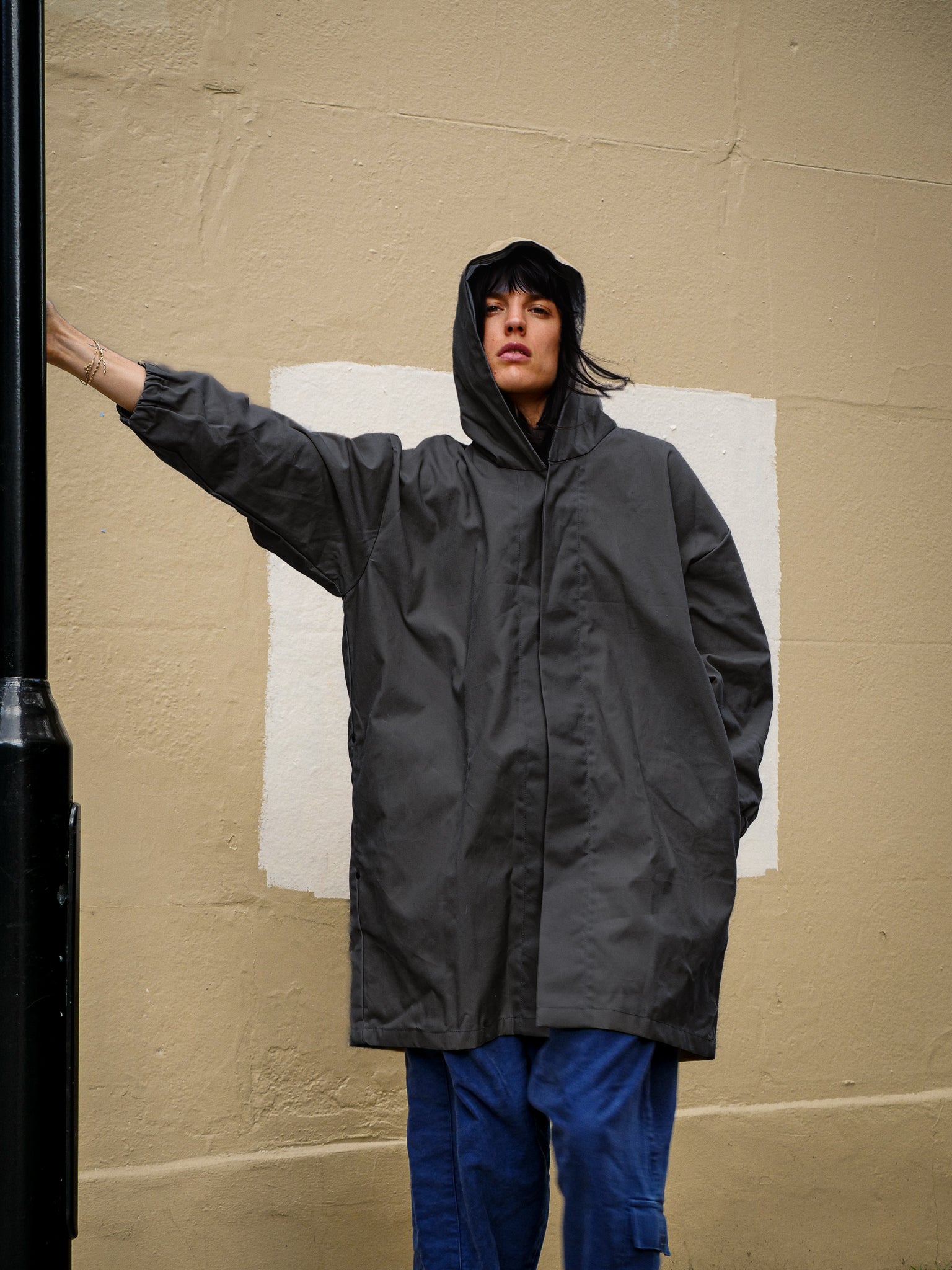 Person wearing a charcoal raincoat against a beige wall