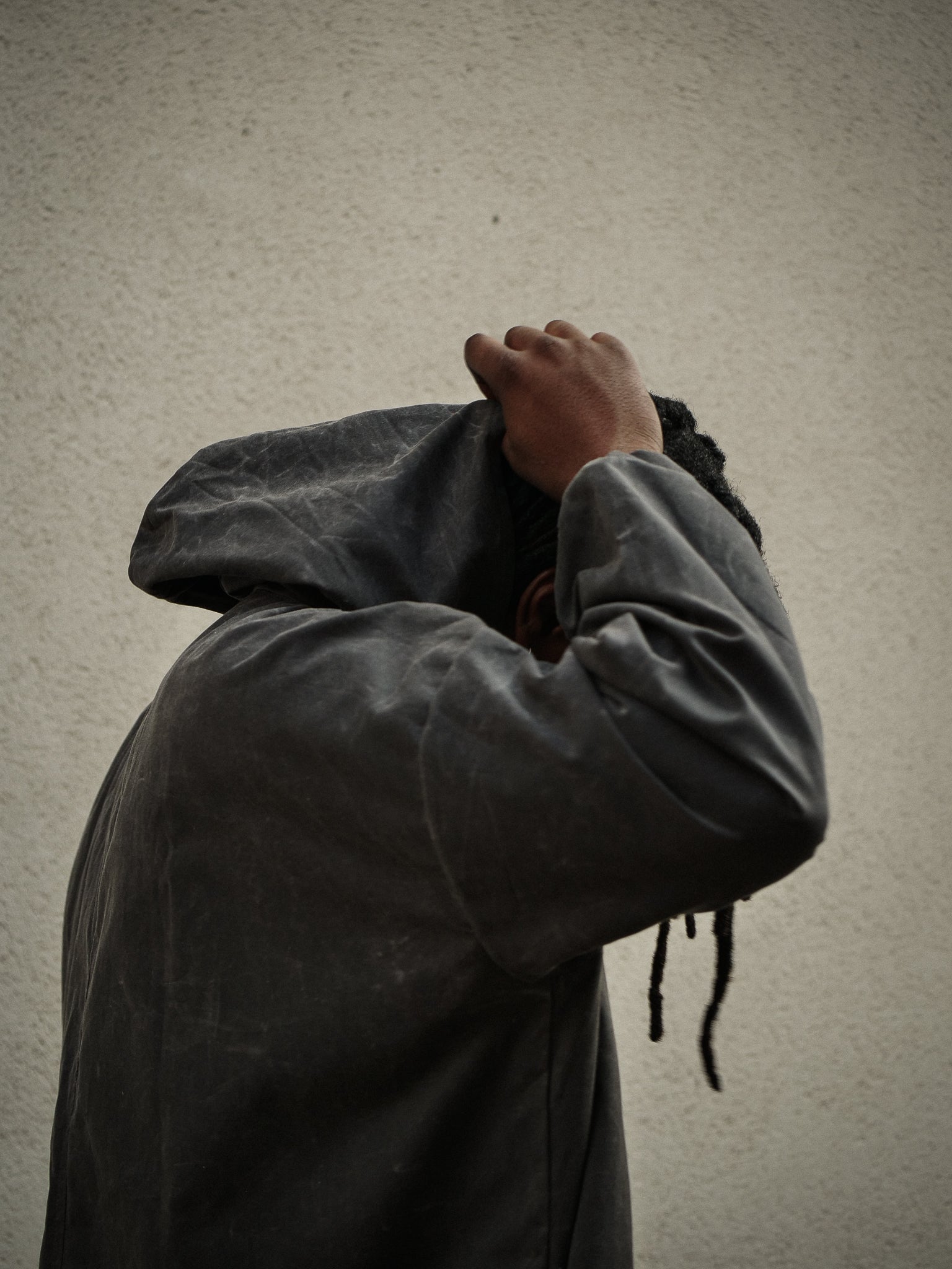 Person wearing a dark jacket with their face obscured against a plain background