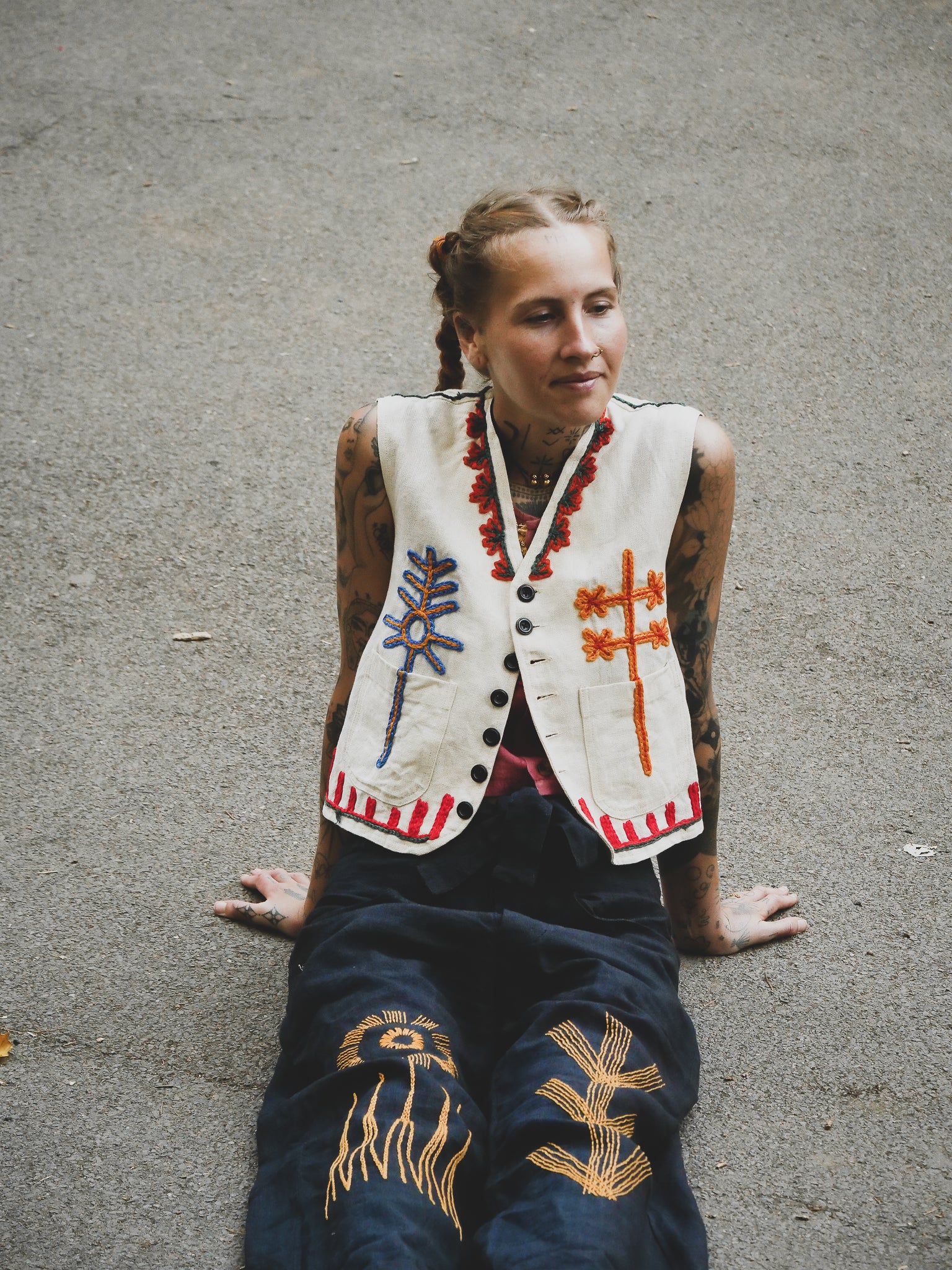 Woman wearing a white embroidered vest and dark blue hand embroidered pants sitting on a concrete surface.