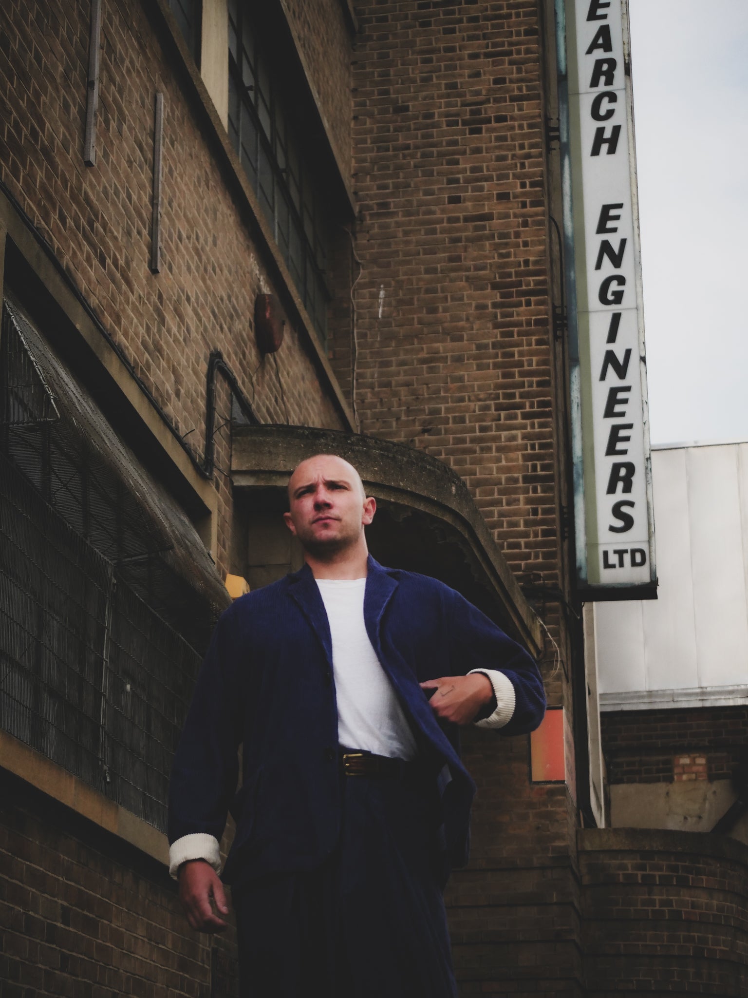 Man standing in front of a brick building with a sign reading 'Research Engineers Ltd'.