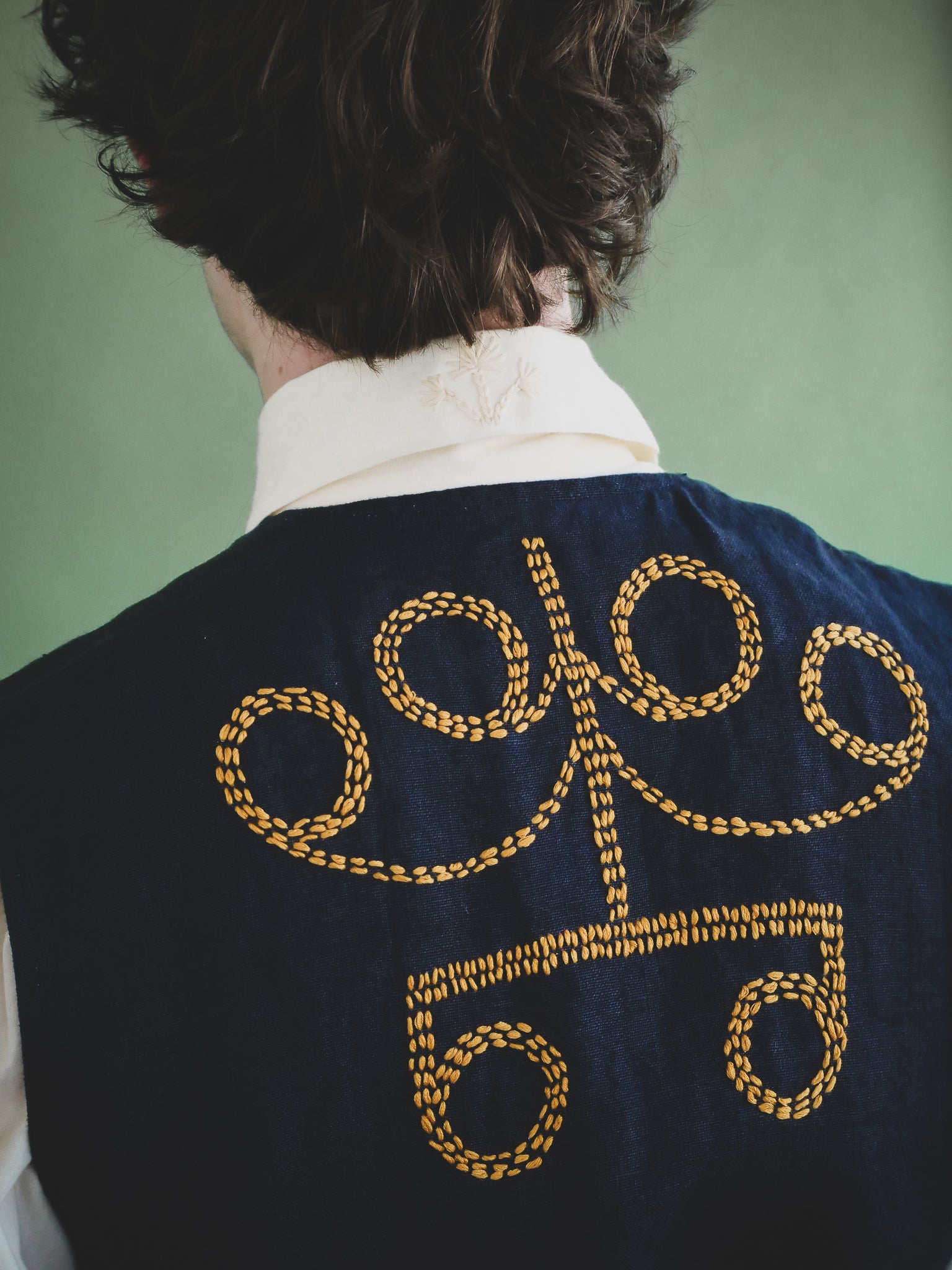 Person wearing a dark blue vest with yellow embroidery on the back against a green background