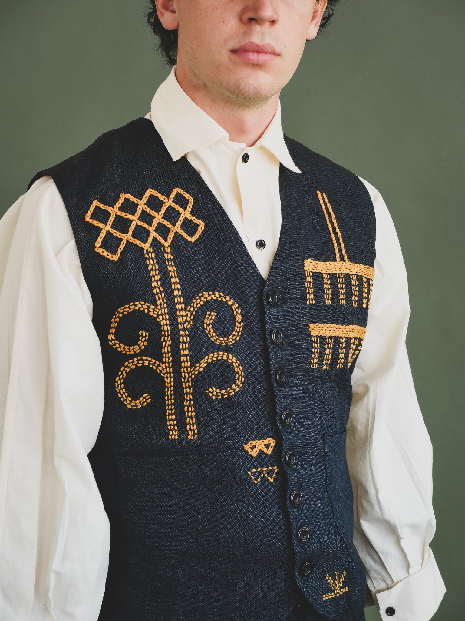 Man wearing a dark blue vest with gold embroidery against a green background