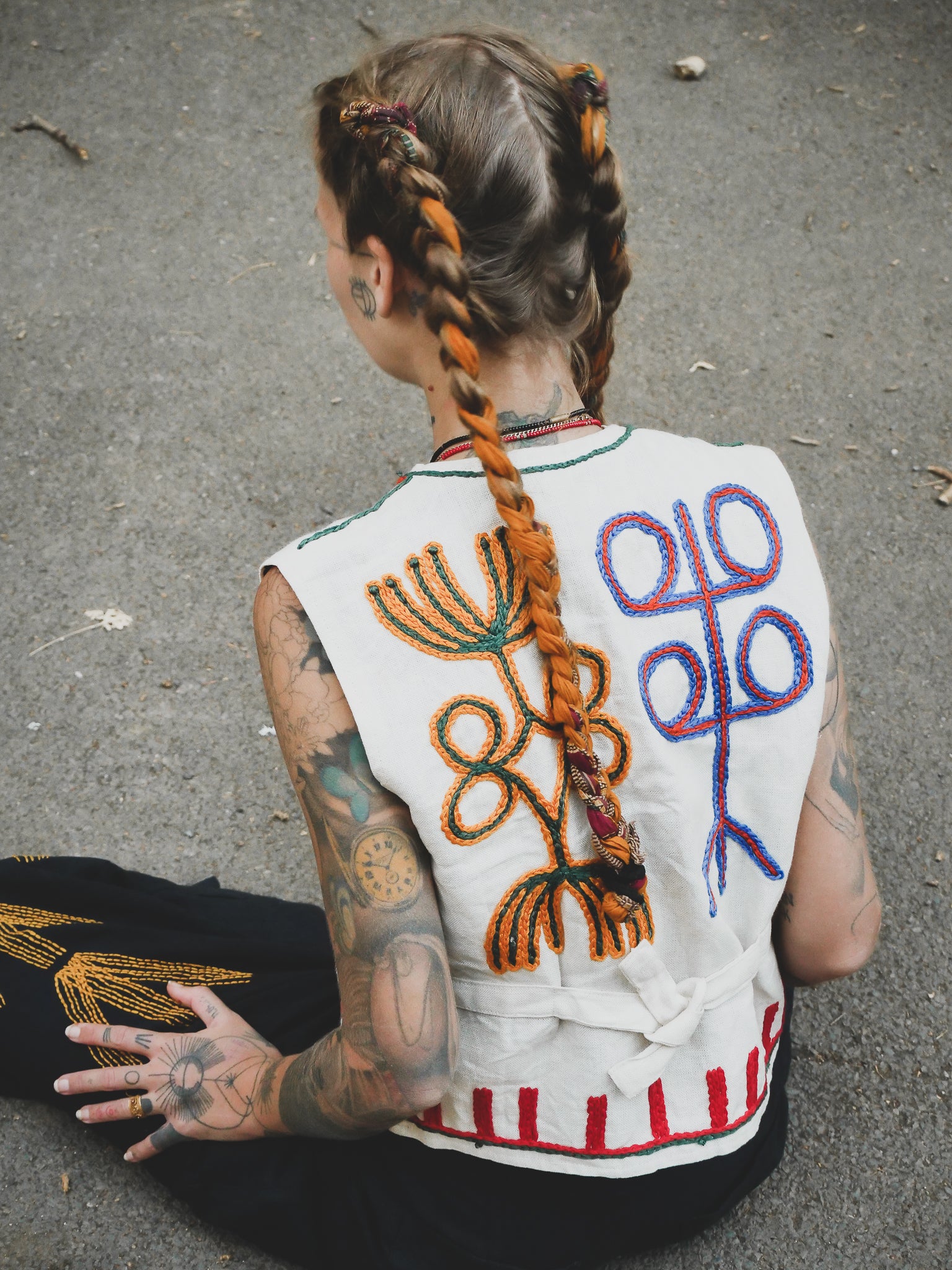 Person wearing a hand embroidered vest with abstract designs on a concrete surface