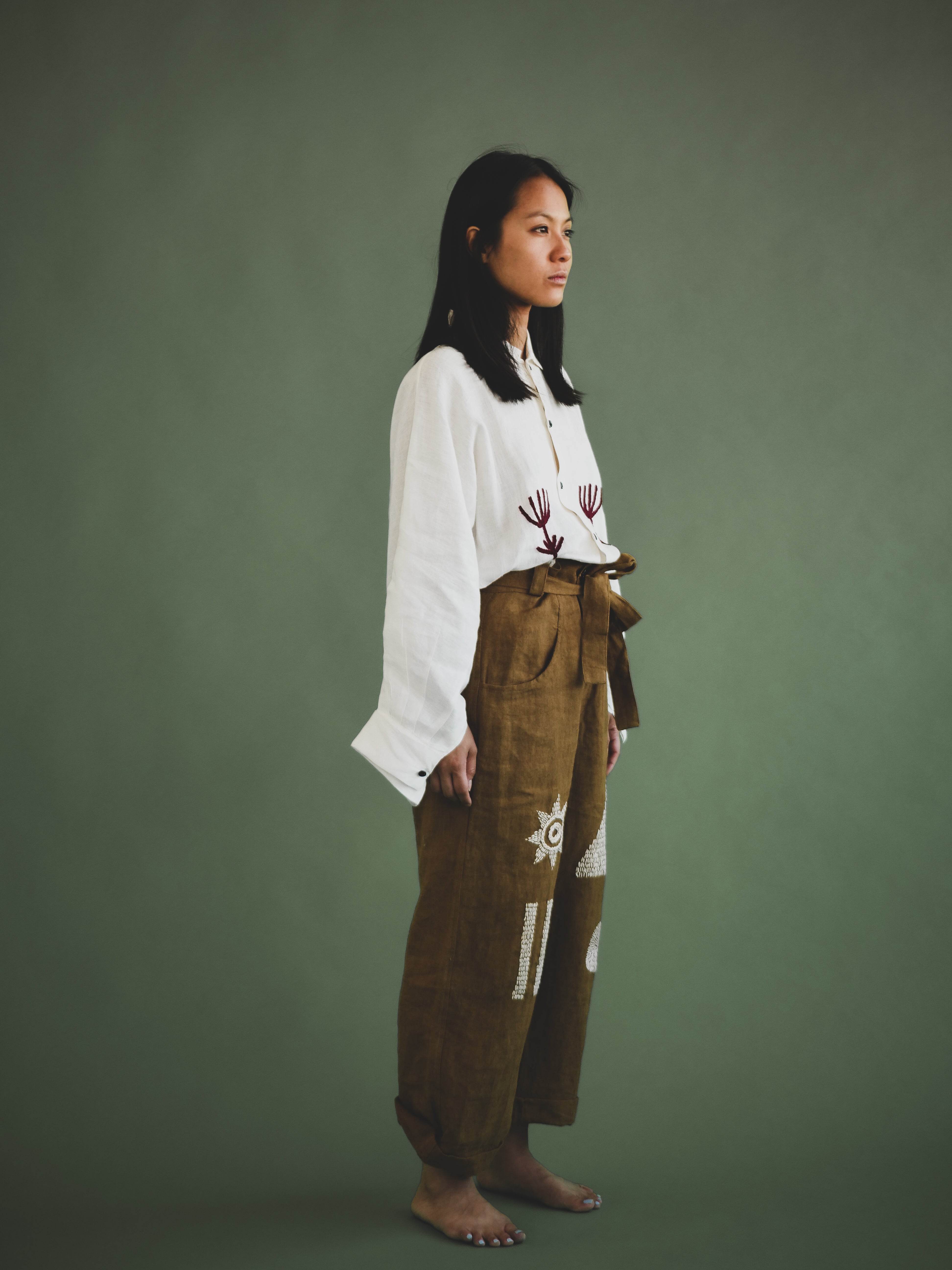 Woman wearing a white top and brown embroidered pants against a green background