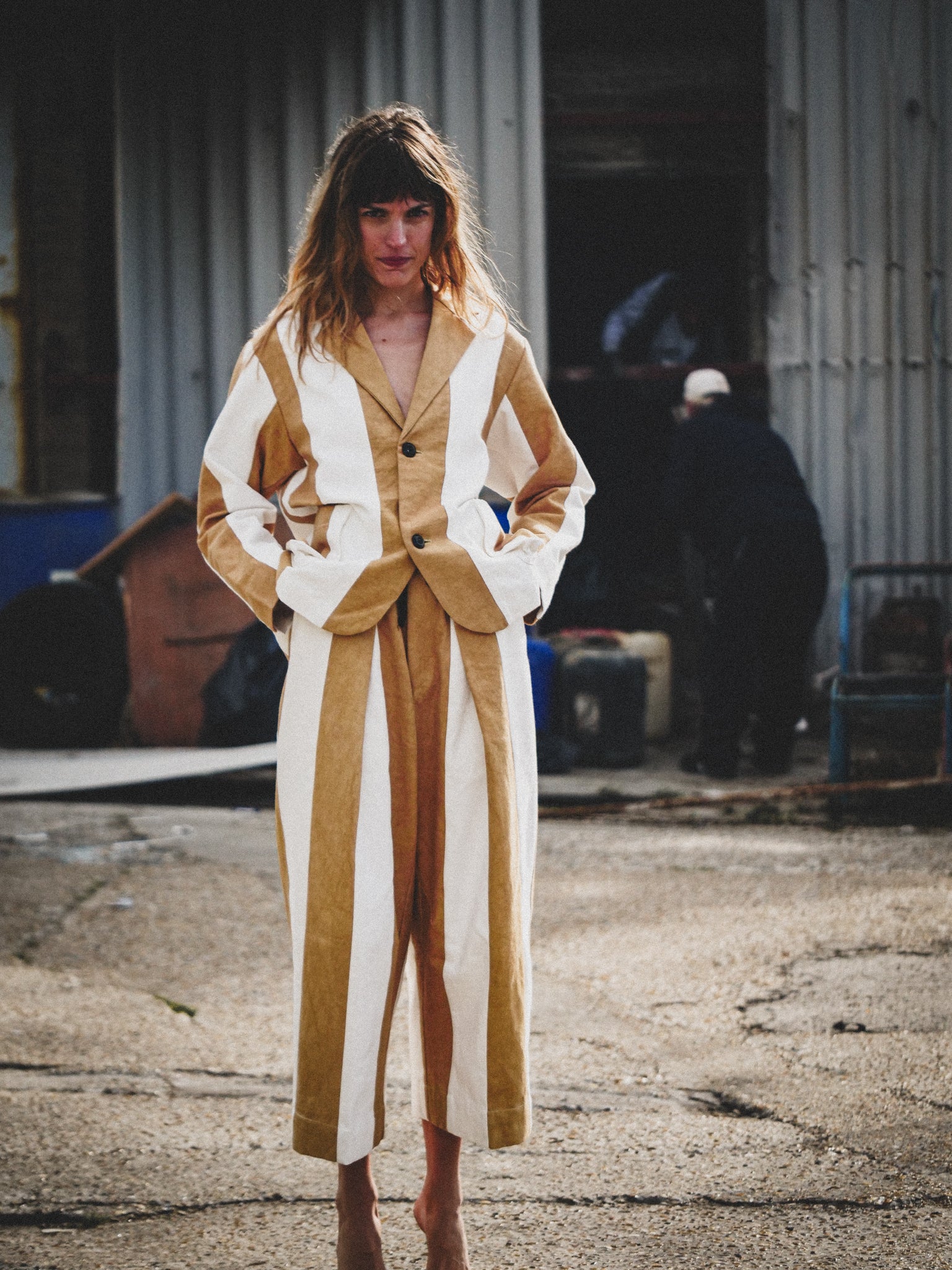 Woman wearing a mustard and white outfit standing in an industrial setting