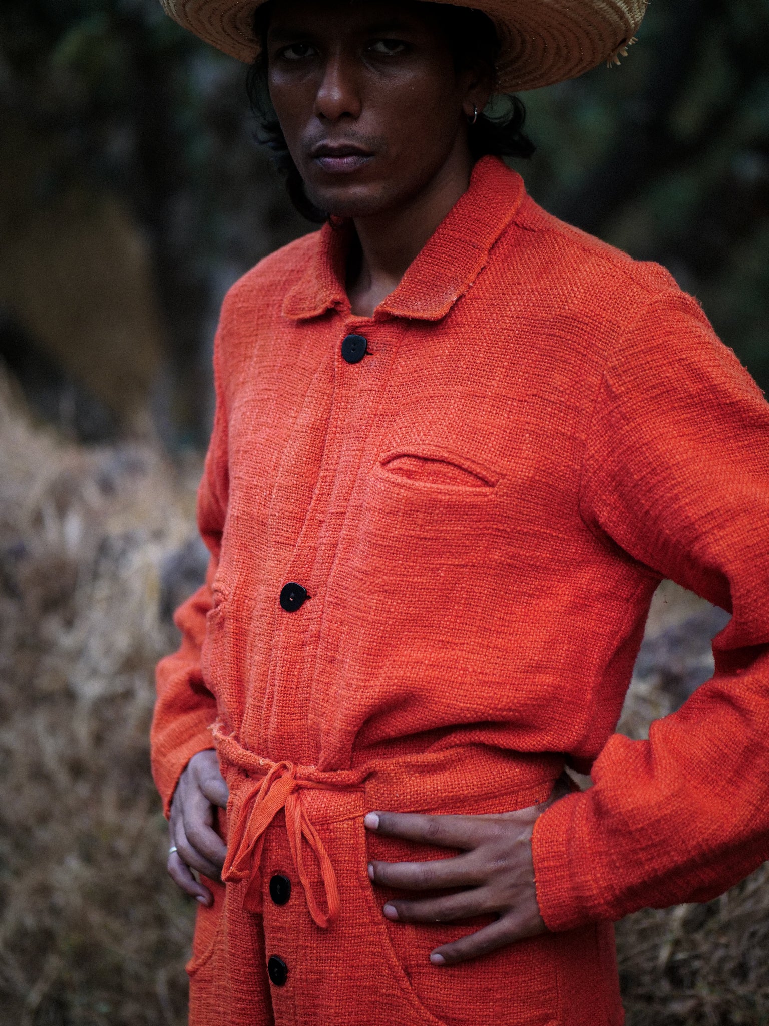 Man wearing an orange coat with a straw hat in a natural setting