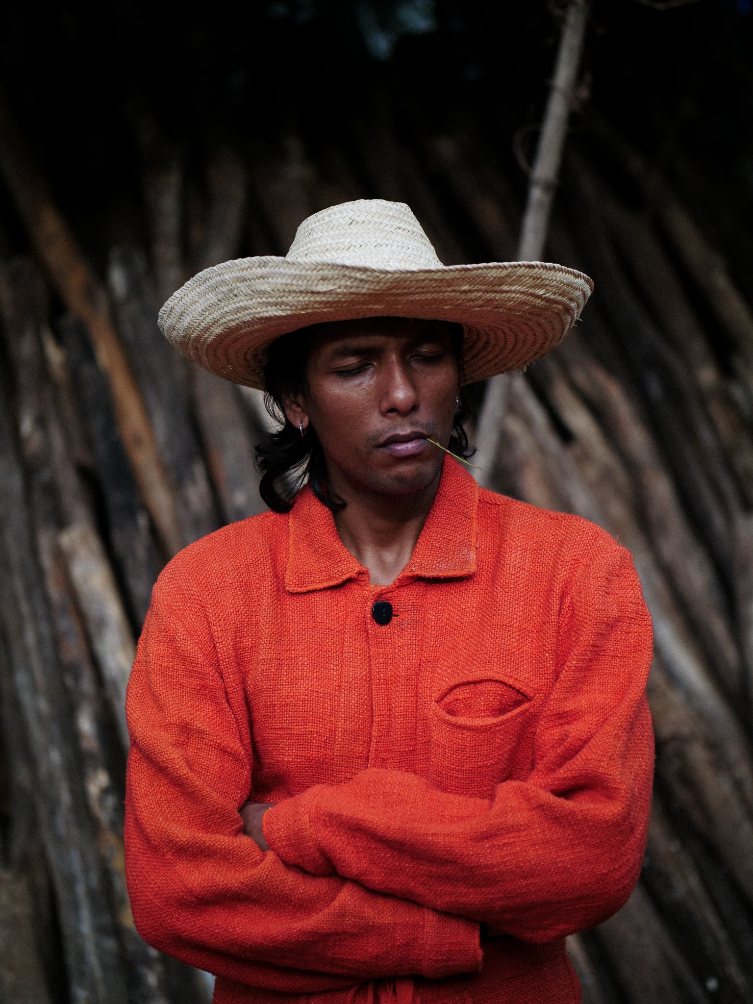 Man in sombrero wearing a red garment and straw hat against a rustic background
