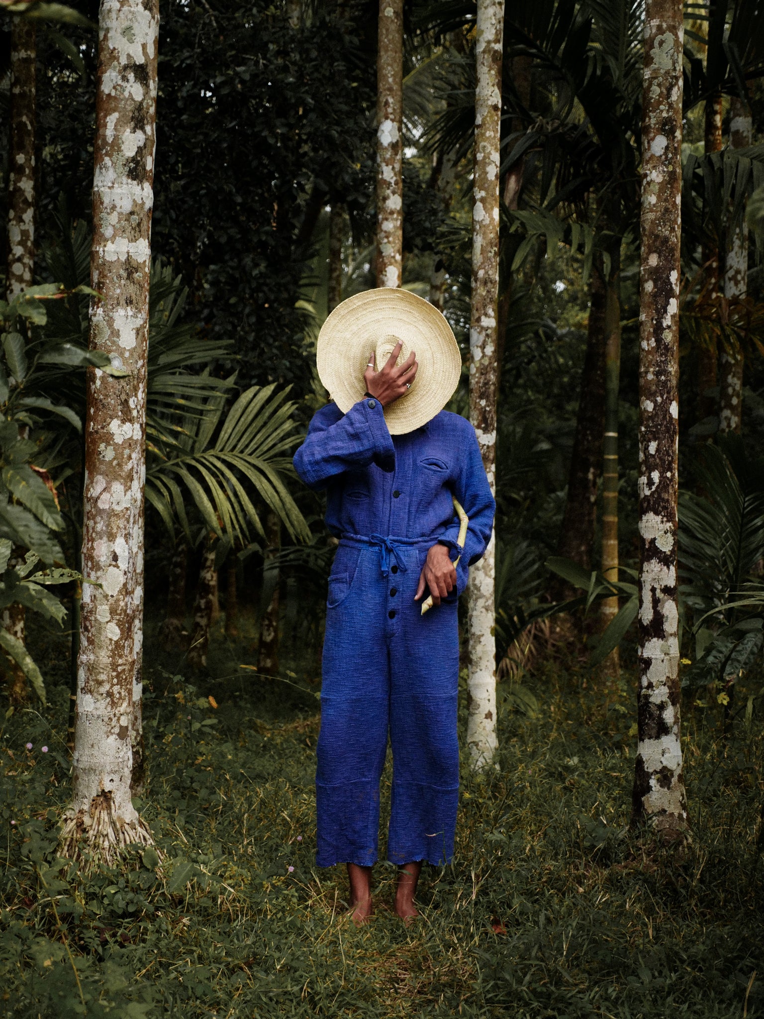 Person in a blue jumpsuit and straw hat standing in a forest