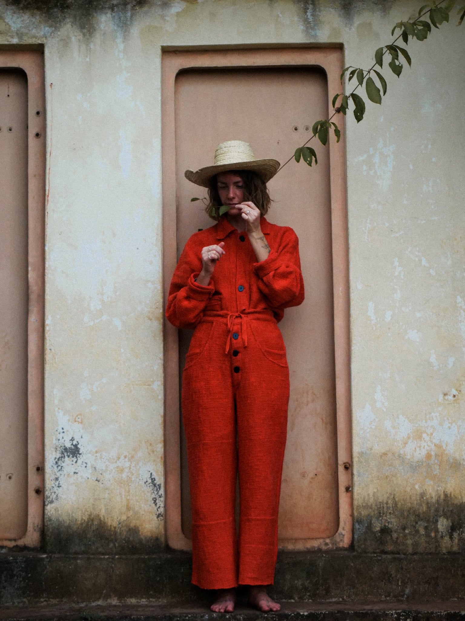 Woman in sombrero wearing an orange jacket and trousers and straw hat standing in a doorway.