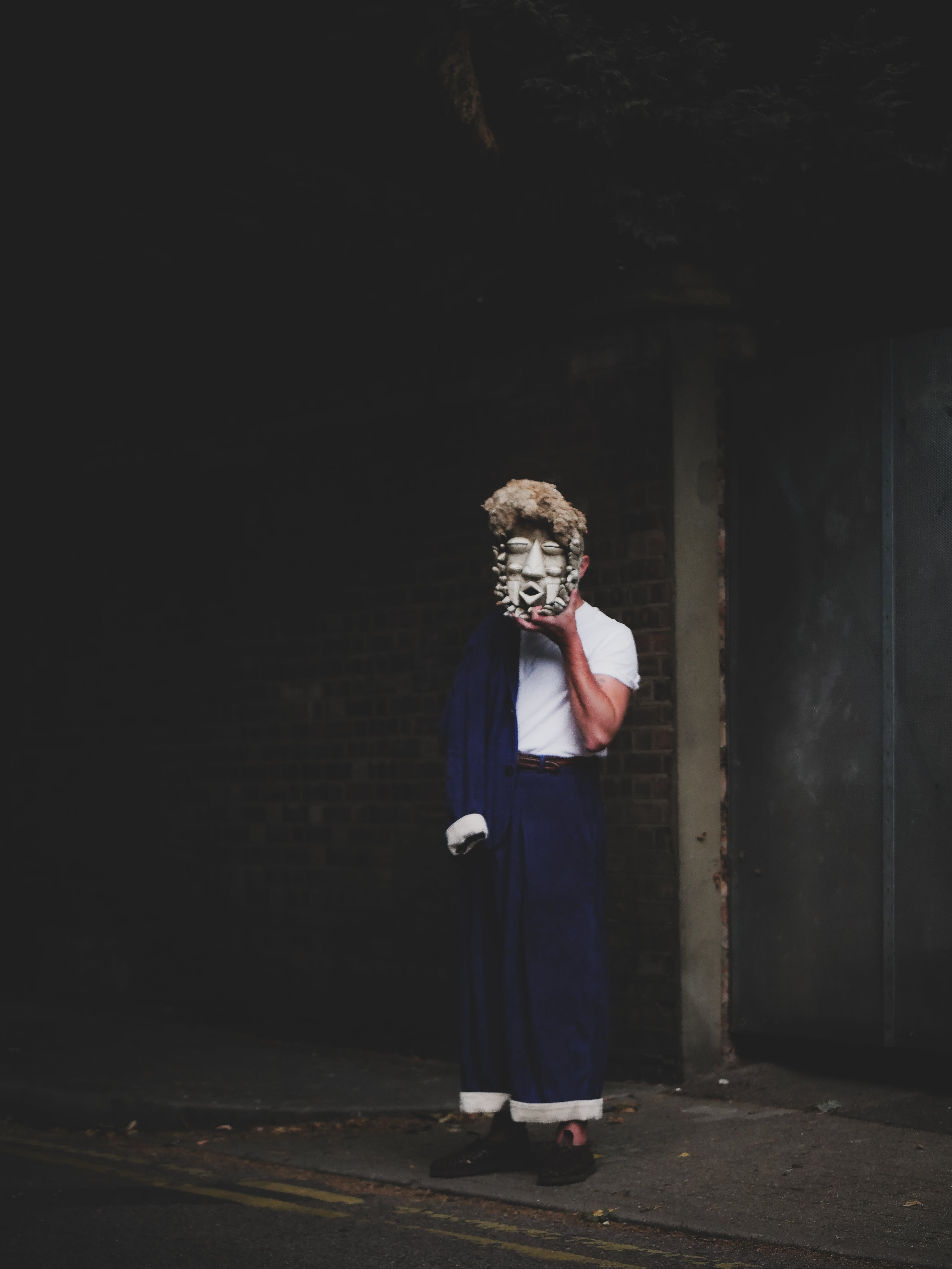 Person wearing a mask and blue outfit in a dark alleyway