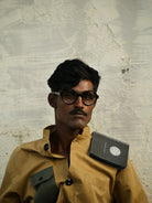 Person wearing a brown jacket with a book on his shoulder against a textured wall.