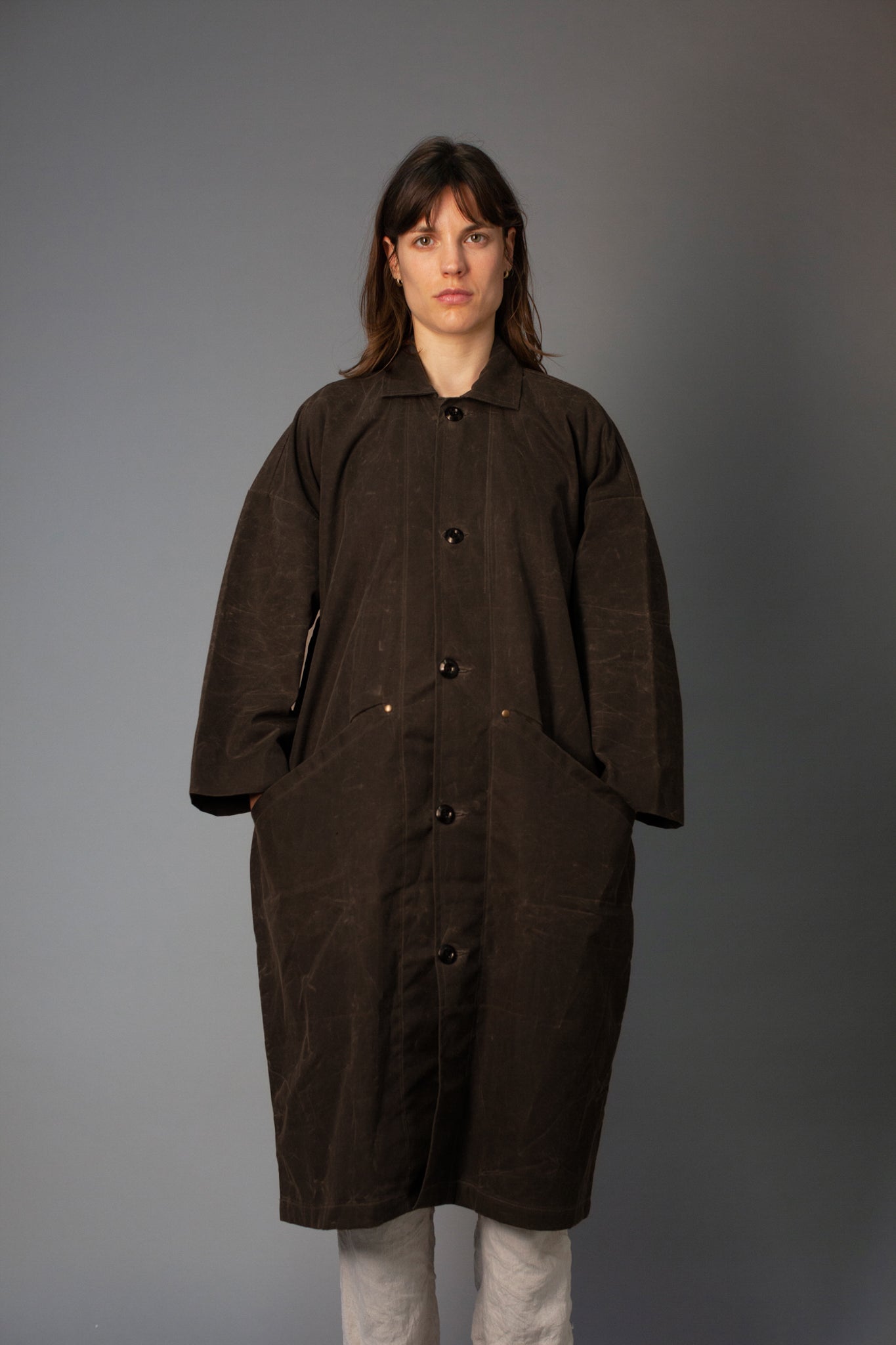 Person wearing a long brown coat against a gray background