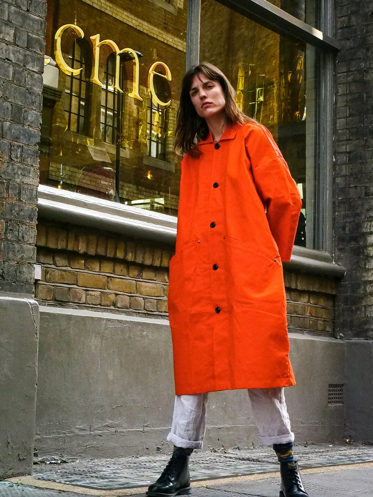 Person wearing an orange coat standing in front of a building with 'cme' branding.