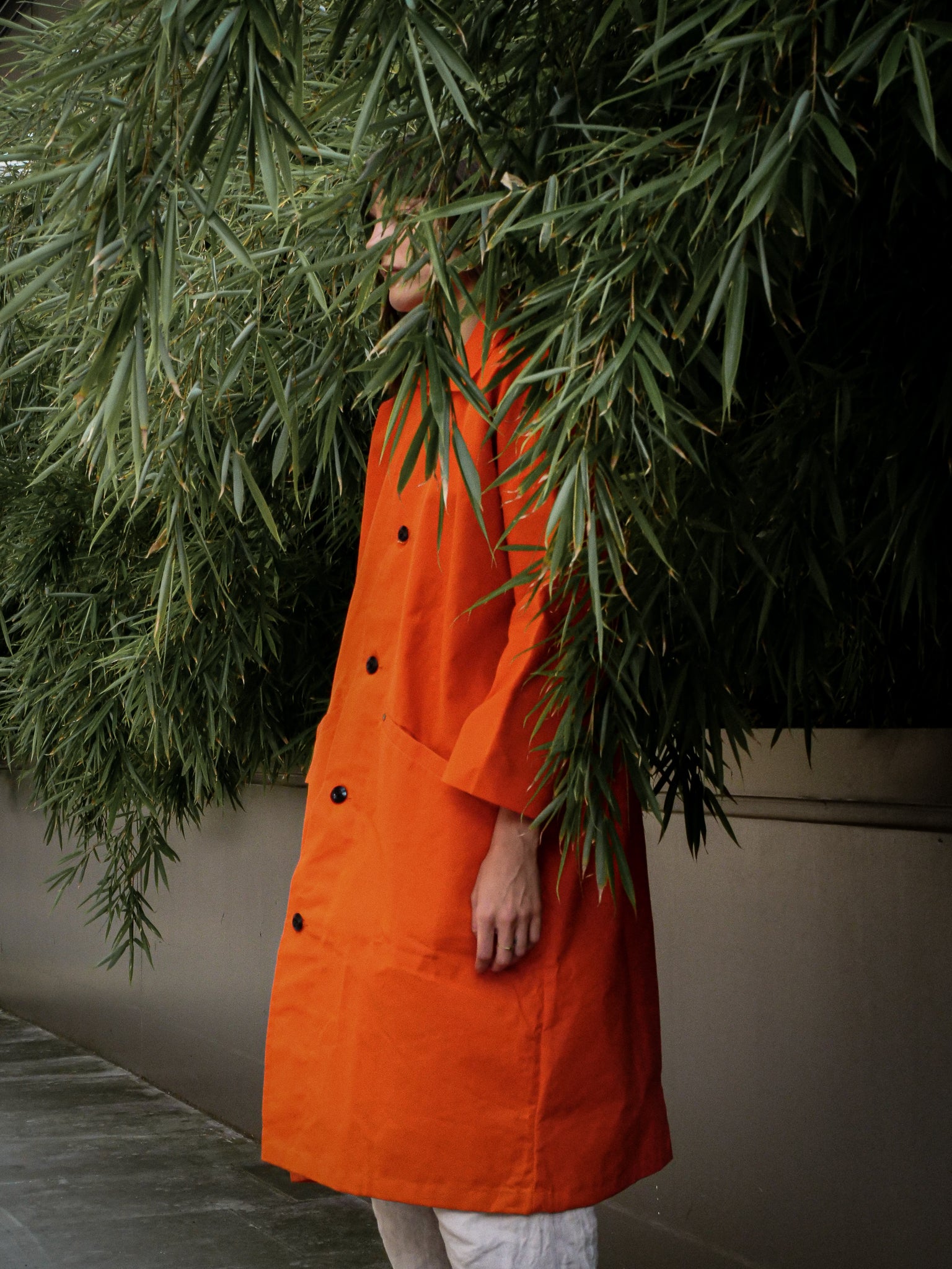 Person wearing an orange coat standing behind green foliage