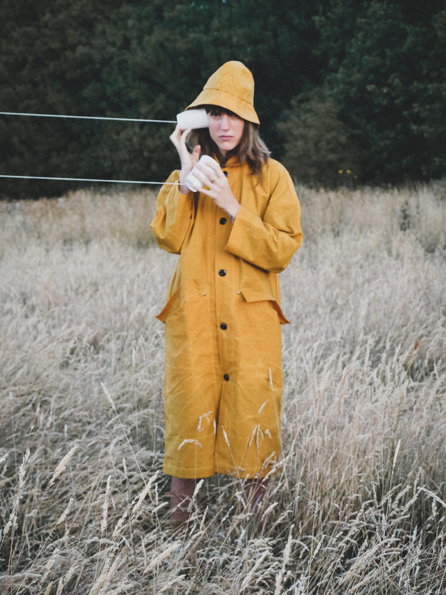 Person wearing a yellow raincoat and hat standing in a field with a blurred background