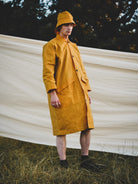 Person wearing a mustard yellow raincoat and hat standing in front of a white fabric backdrop.