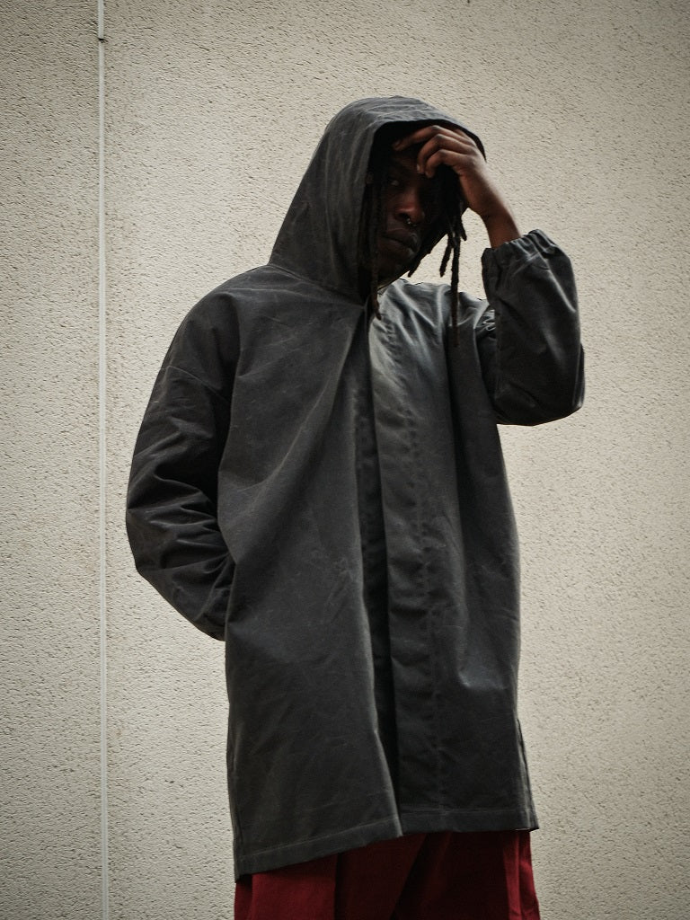Person wearing a dark raincoat against a plain wall