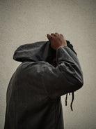 Person wearing a dark jacket with their face obscured against a plain background