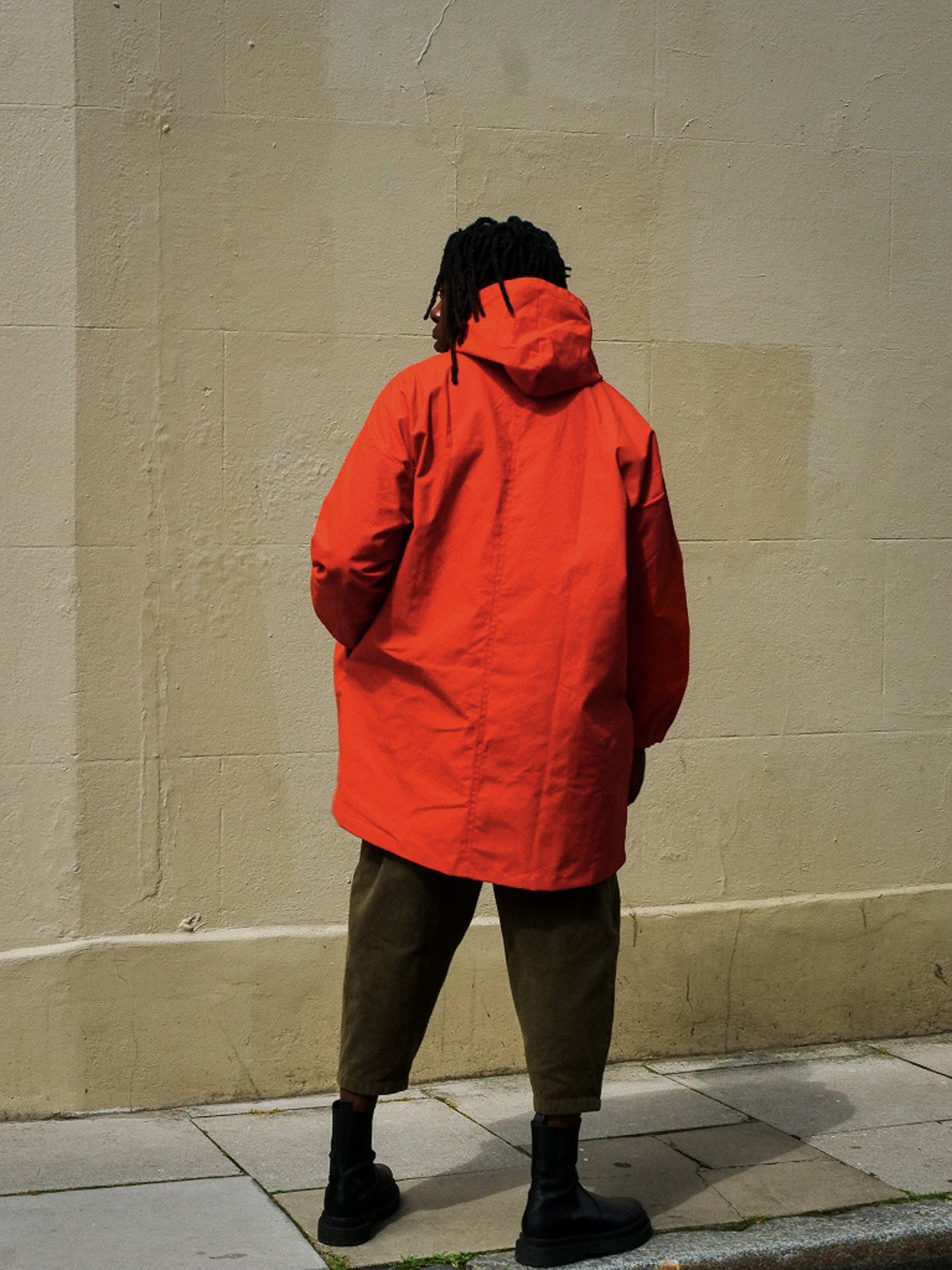 Person wearing a bright orange raincoat standing against a beige wall.