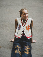 Woman wearing a white embroidered vest and dark blue hand embroidered pants sitting on a concrete surface.
