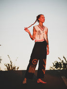 Person wearing a sleeveless top and pants with decorative patterns against a natural background