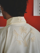 Person wearing a off-white shirt with gold embroidery against a red wall.