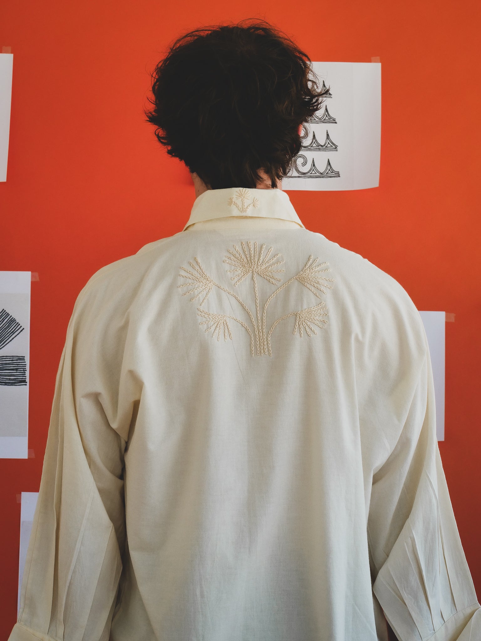 Person wearing an off-white embroidered shirt against an orange wall with prints.
