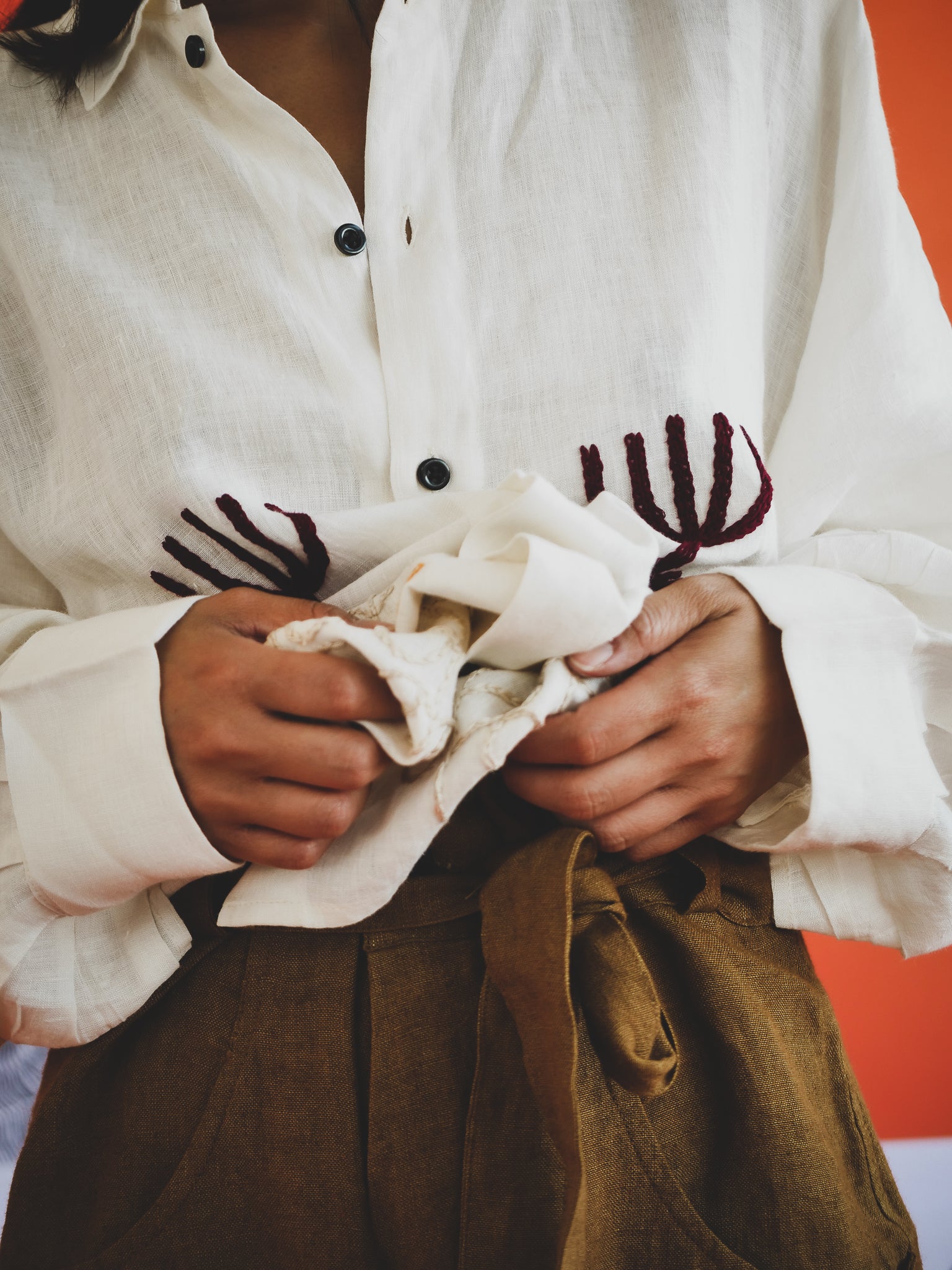 Person wearing a white shirt hand embroidery, holding a piece of fabric.