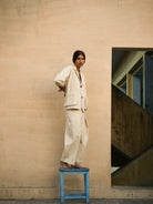 Person in a beige suit standing on a blue stool against a beige wall.