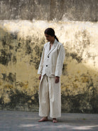 Person wearing a beige suit standing against a textured wall.