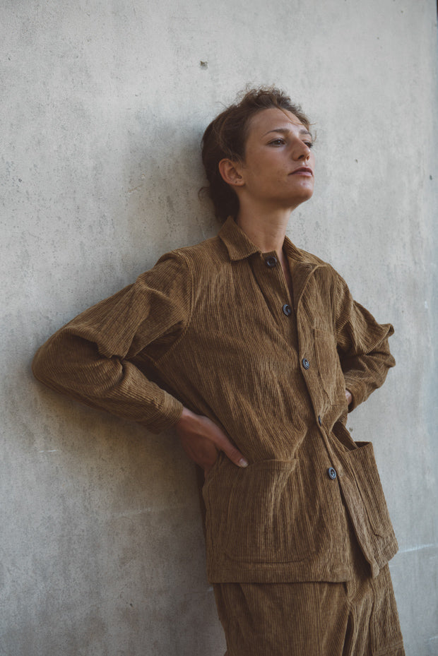 Person wearing a brown corduroy outfit against a concrete wall.