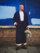 Person wearing a blue blazer and holding a patterned bag against a blue wall and brick wall.