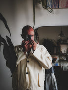 Person taking a mirror selfie wearing a beige coat in a room with a mirror and various items on the wall.