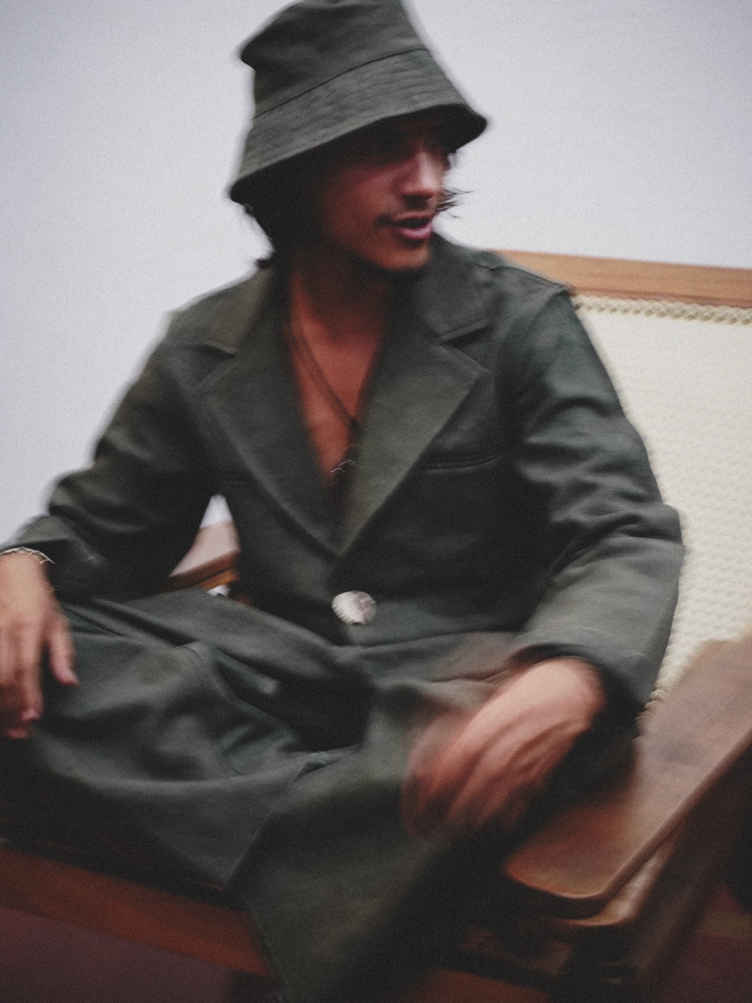 Person wearing a dark green jacket and hat sitting on a couch.