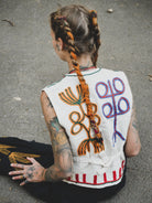 Person wearing a hand embroidered vest with abstract designs on a concrete surface