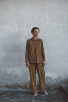 Person wearing a brown corduroy outfit standing against a textured wall.