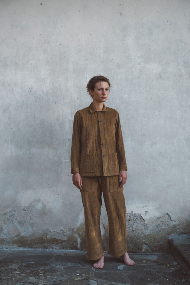 Person wearing a brown corduroy outfit standing against a textured wall.