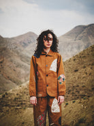 Person wearing a brown jacket with patterned patches in a mountainous landscape