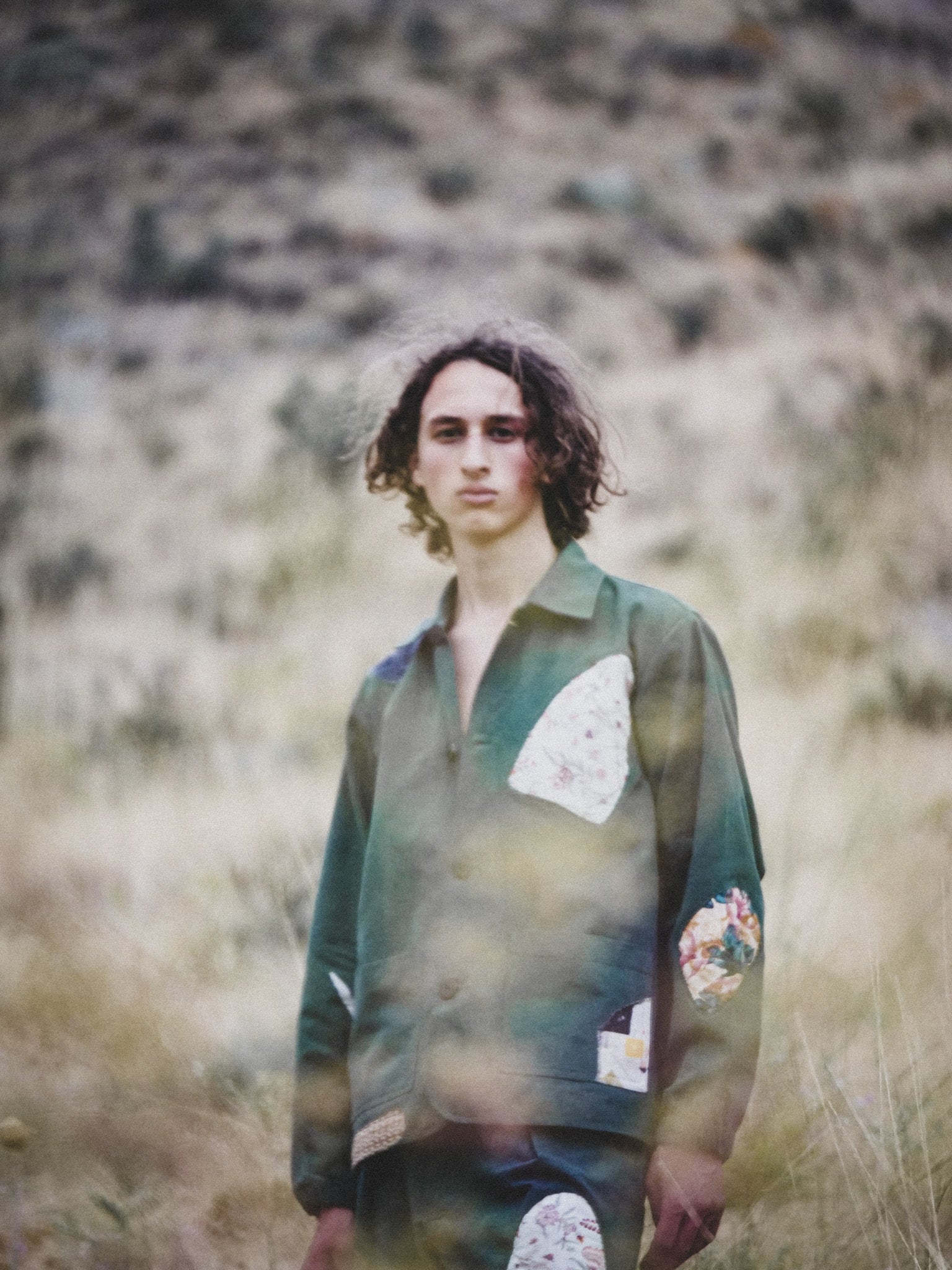 Person wearing a green jacket with patterned patches in a natural setting