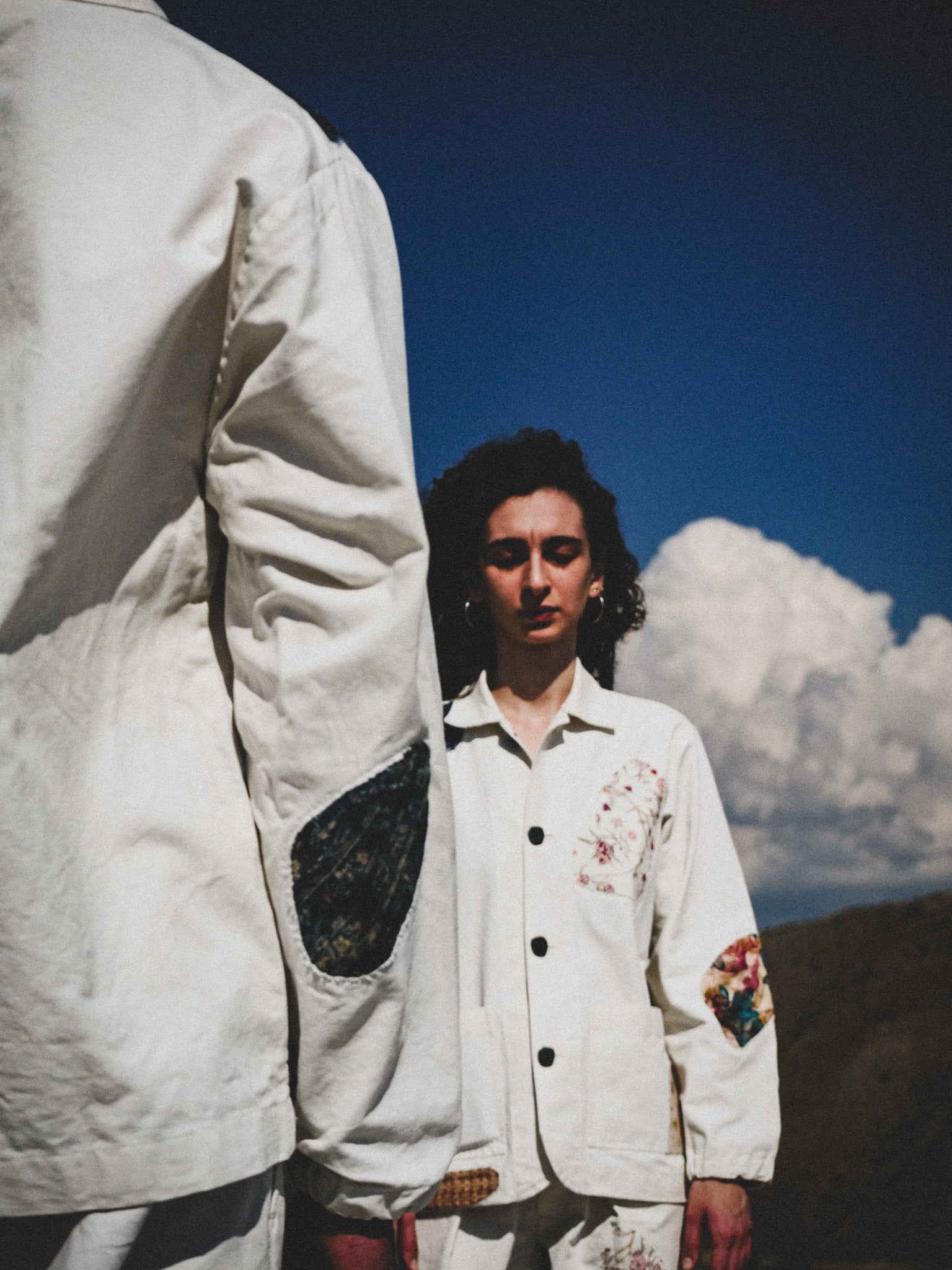 Person wearing a white jacket with floral designs against a mountainous landscape