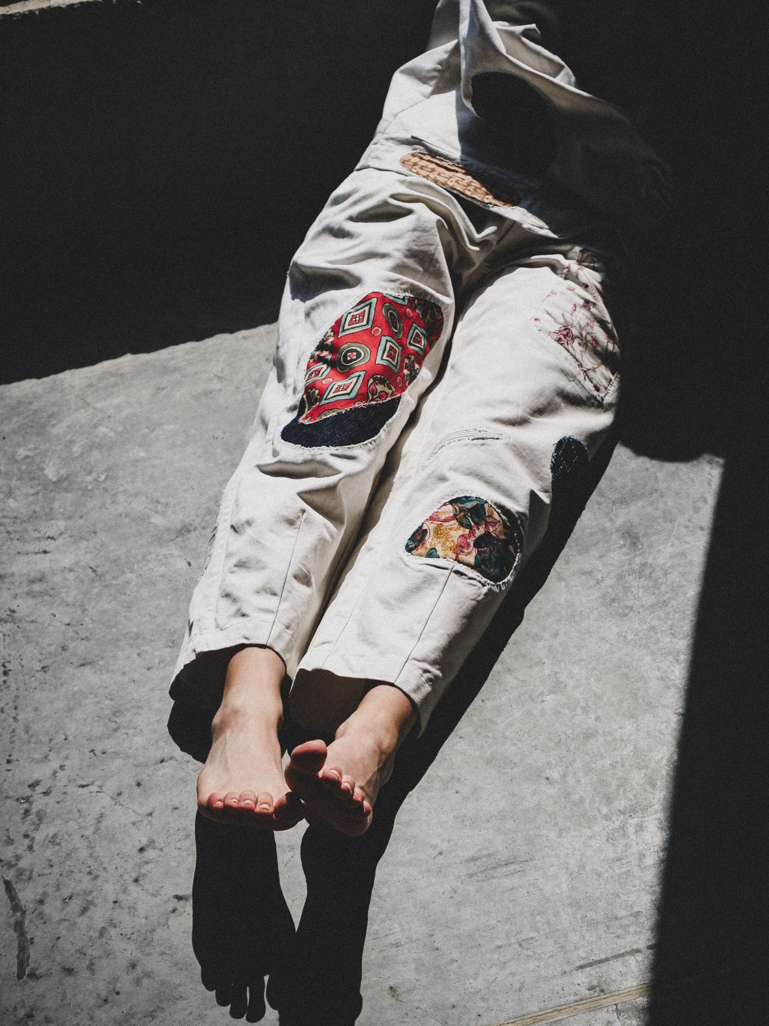 Person wearing a white trousers with colorful patches on a concrete surface