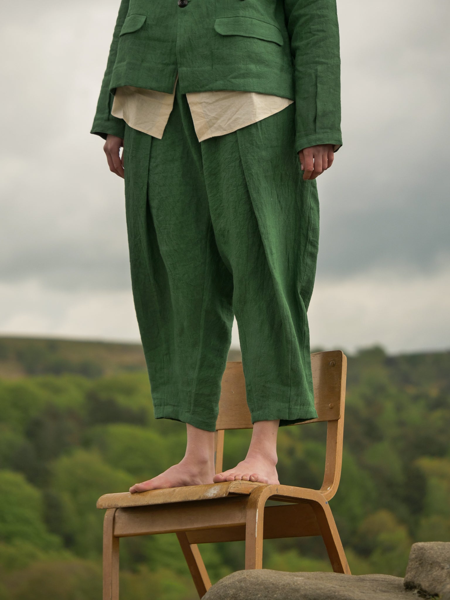 Person wearing a green outfit standing on a wooden chair with a natural landscape in the background