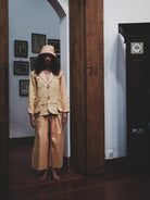 Person wearing a pale mustard suit standing in a room with wooden doors and framed pictures on the wall.