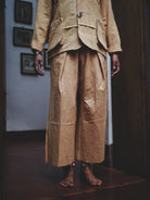 Woman wearing a pale mustard suit in a room with framed pictures on the wall.