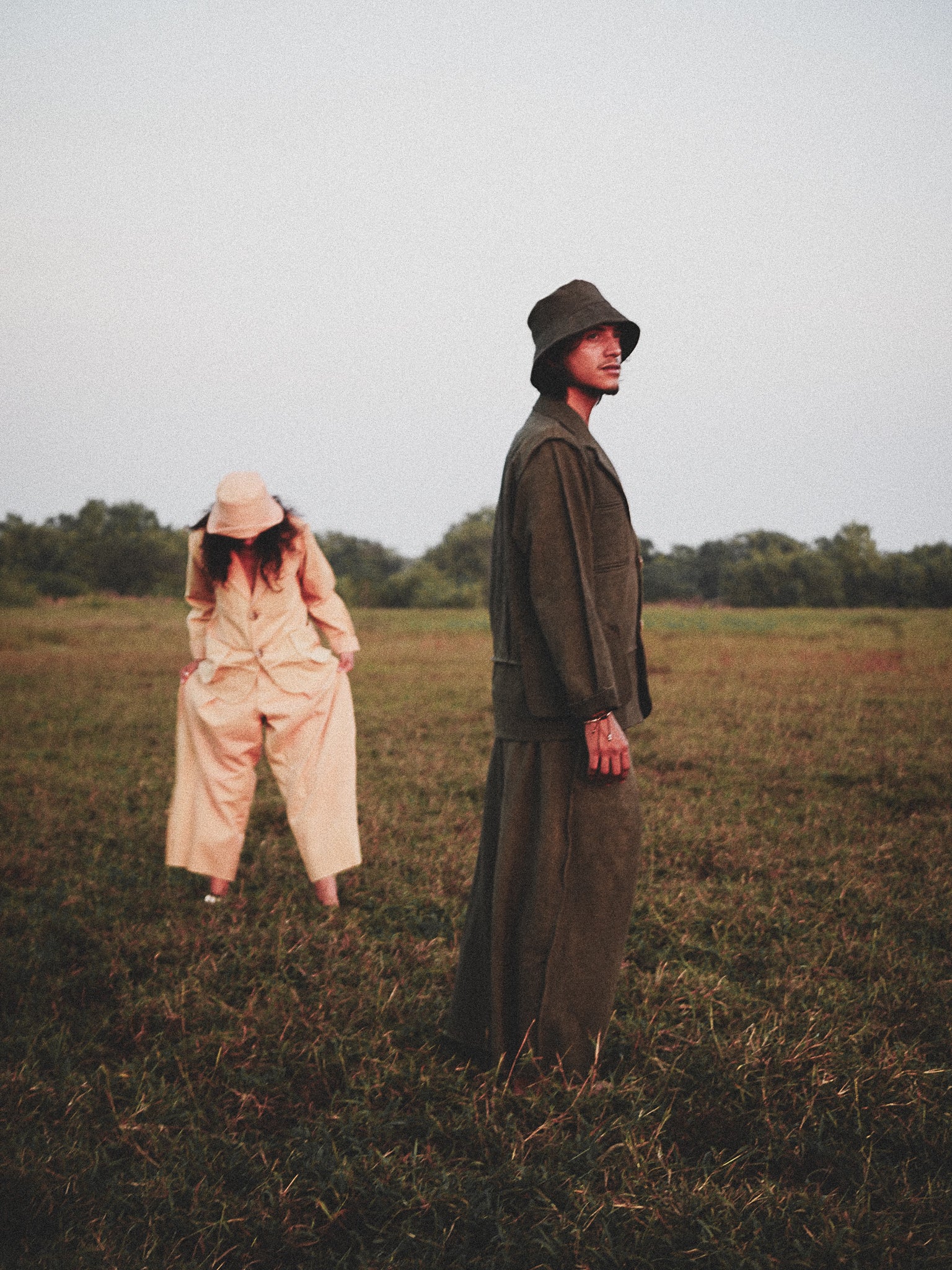 Two people standing in a field wearing canvas clothing.
