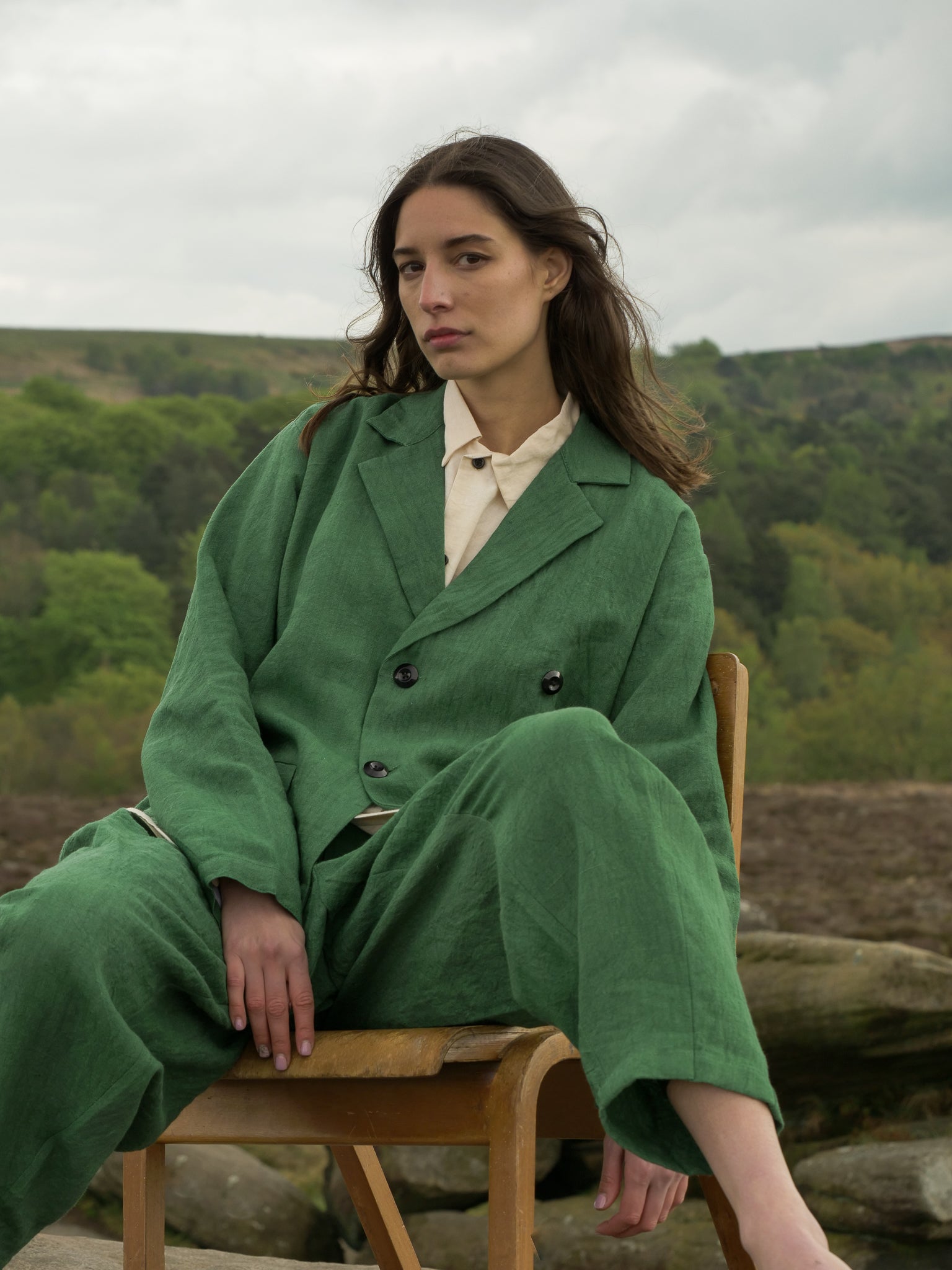 Woman in a green coat sitting on a wooden chair with a natural landscape in the background