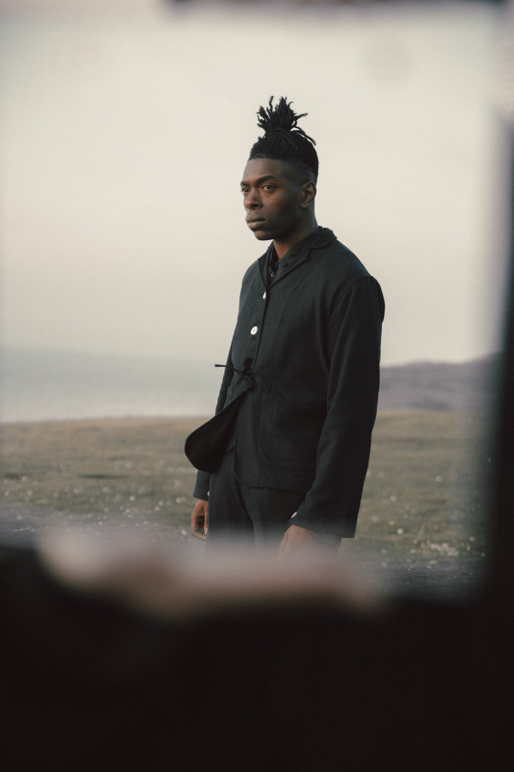 Man in a black jacket standing in a field with a blurred foreground