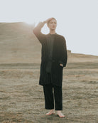 Person wearing a dark outfit standing in a desert landscape with a sunlit sky.