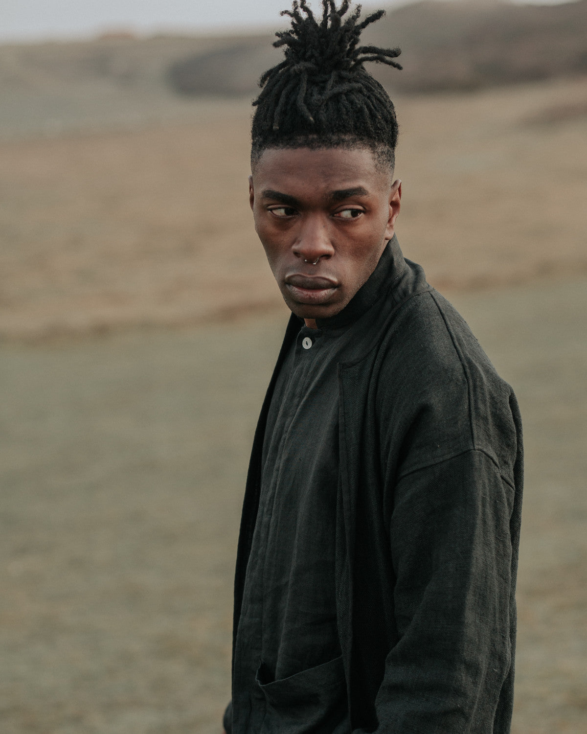 Man with styled hair wearing a dark jacket in a desert-like setting